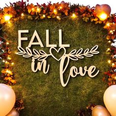 fall in love sign surrounded by balloons and garlands with lights on the grass behind it