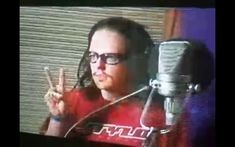 a woman with glasses is giving the peace sign in front of a microphone and television screen