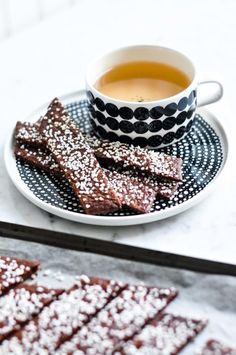 powdered sugar coated brownies on a plate next to a cup of tea