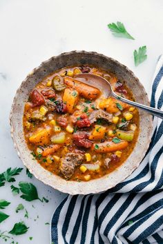 a bowl filled with vegetable soup on top of a blue and white striped towel next to a spoon