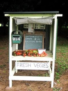 a sign that says fresh veggies in front of a stand with fruit on it