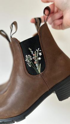 a person is holding on to some brown boots with flowers painted on the soles