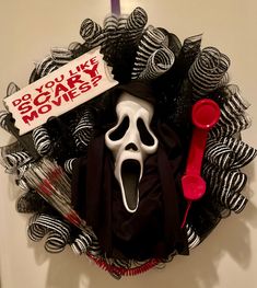 a wreath decorated with black and white halloween decorations, including a scream mask on it