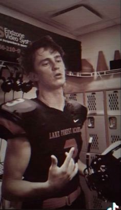 a young man in a football uniform is talking to someone on the tv screen with his hand up