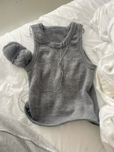 a gray sweater and some balls of yarn on a bed