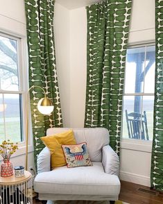 a living room with green and white curtains, a gray chair, and a yellow throw pillow