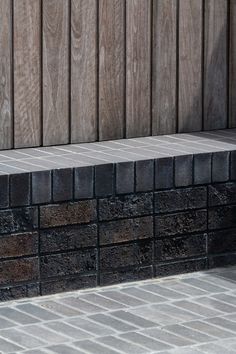 a black and white cat sitting on the ground next to a brick wall with a wooden fence behind it