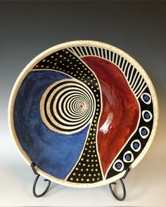 a decorative bowl is sitting on a metal stand with an abstract design in the center