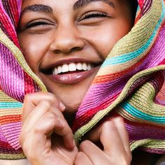 a smiling woman wearing a colorful scarf on her head and holding hands under her chin