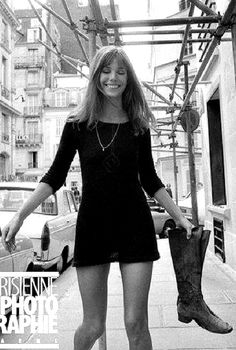 black and white photograph of a woman in short dress holding an umbrella on the sidewalk