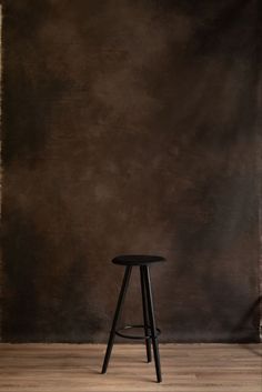 a black stool sitting on top of a hard wood floor next to a brown wall