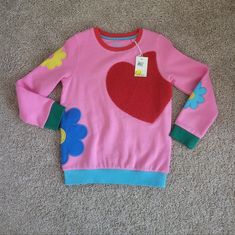 Heavy Pink Sweatshirt Has Multi-Colored Bands, Red Neck, Green Cuffs, And A Blue Banded Waist. The Front Has An Oversized Heavy Red Heart Applique, With Heavy Mod Flower Appliques On Both Sleeves And The Left Side That Wraps Around To The Back. Made Of A Soft Cotton Blend. Size 7/8 Would Look Awesome Paired With Her Favorite Jeans Or Skirt Nwt Never Worn Excellant Condition No Damage Boden Playful Multicolor Long Sleeve Sweatshirt, Playful Winter Sweatshirt For Playwear, Cute Pink Patchwork Tops, Playful Pink Crew Neck Sweater, Pink Patchwork Tops For Fall, Playful Long Sleeve Sweatshirt For Playwear, Playful Pink Sweatshirt For Playtime, Playful Long Sleeve Playwear Sweatshirt, Playful Long Sleeve Cotton Sweater