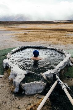 a man in a blue hat swims in a large body of water surrounded by rocks