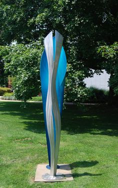 a large metal sculpture sitting on top of a lush green field next to a tree