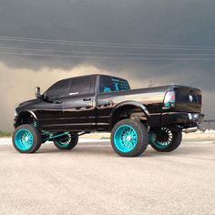 a black truck with turquoise rims parked in front of a dark cloud filled sky