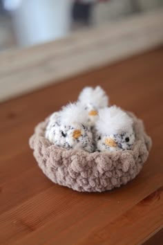 two small white birds sitting in a crocheted basket on a wooden counter top