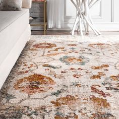 a white rug with an orange and blue floral design on the floor next to a couch