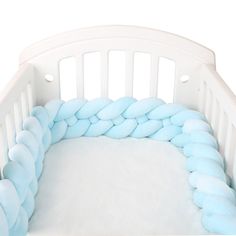 a white crib with blue pillows on it's sides and a pillow in the middle