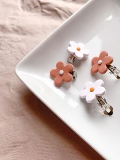 three little flower clips are sitting on a white plate with pink and white flowers in them