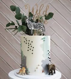 there is a cake decorated with animals and greenery on the top tier, which reads wild