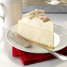 a piece of cheesecake on a white plate with a fork and cup in the background