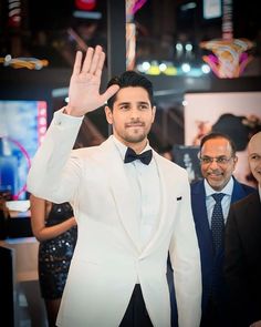 a man in a tuxedo waves at the camera while standing next to other men