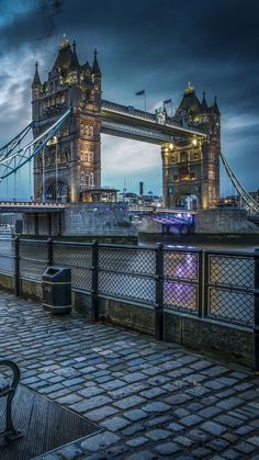 a bench sitting on the side of a river next to a tall tower bridge at night