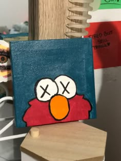 a painting of an angry bird is displayed on a wooden block in front of a stack of books