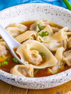 a white bowl filled with dumplings and soup on top of a wooden table next to a spoon