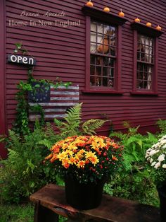 an open sign and flowers in front of a red building