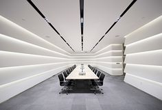 an empty conference room with long tables and chairs in the center is lit by recessed lighting