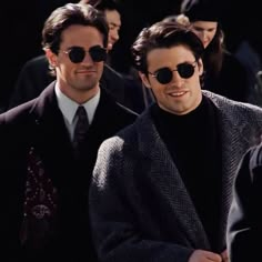 two men in suits and sunglasses are walking down the street with other people behind them