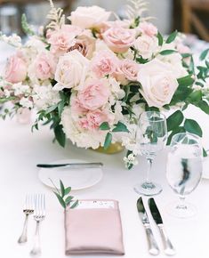 the table is set with pink and white flowers in vases, silverware, and napkins