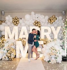 a man and woman standing in front of a sign that says marry me with balloons