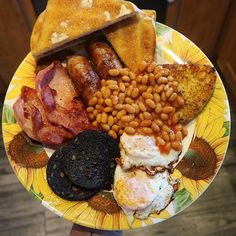 a plate full of breakfast foods including eggs, bacon, toast and beans on it