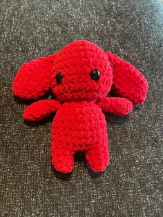 a red crocheted stuffed animal laying on top of a gray carpeted floor