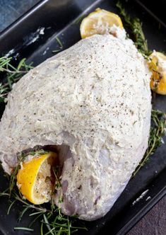 a raw chicken with herbs and lemons on a black tray, ready to be cooked