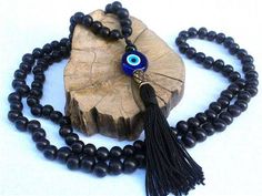 a black beaded necklace with an evil eye and tasseled cord on a piece of wood