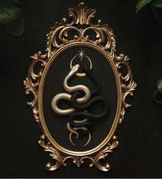 an ornate gold frame with a snake in the center on a black background and greenery behind it