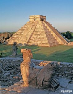 an ancient building in the middle of a grassy area with ruins and statues around it