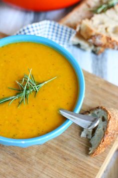 a blue bowl filled with soup next to bread on a cutting board and an orange bowl in the background