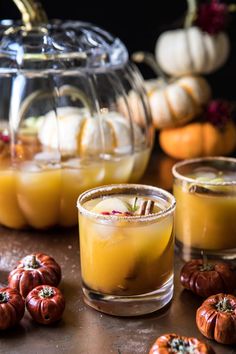 two glasses filled with liquid sitting on top of a table next to small pumpkins