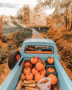 an old blue truck filled with pumpkins driving down a country road in the fall