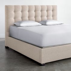 an upholstered bed with white sheets and pillows