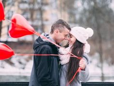 a man and woman standing next to each other with red balloons in front of them