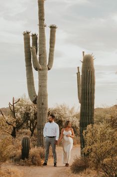 a man and woman holding hands while walking in front of a large saguado