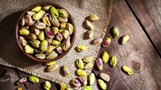 a wooden bowl filled with pistachios on top of a table