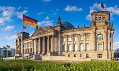 an old building with a flag flying in front of it and people walking around outside