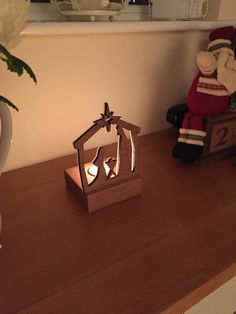 a wooden candle holder with two lit candles in the shape of a house and a nativity scene