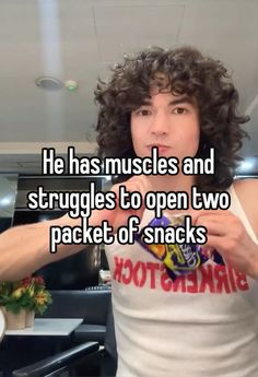 a man with curly hair pointing at the camera while wearing a tank top that says he has muscles and struggles to open two packet of snacks